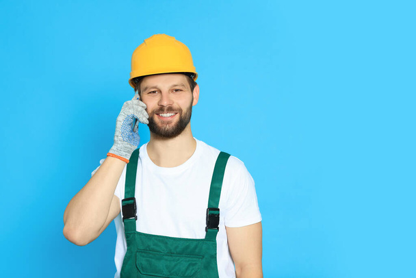 Professional repairman in uniform talking on smartphone against light blue background. Space for text - Foto, Imagem