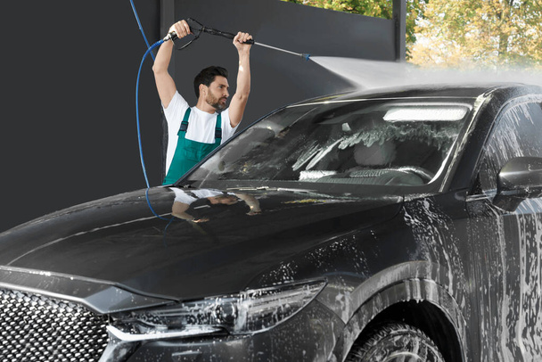 Worker washing auto with high pressure water jet at outdoor car wash - Foto, immagini