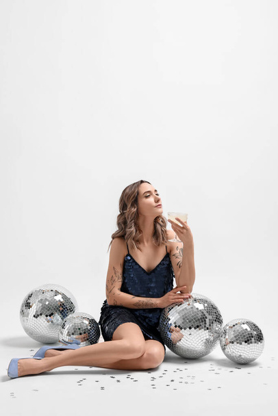 Beautiful woman with glass of drink and disco balls on white background - 写真・画像