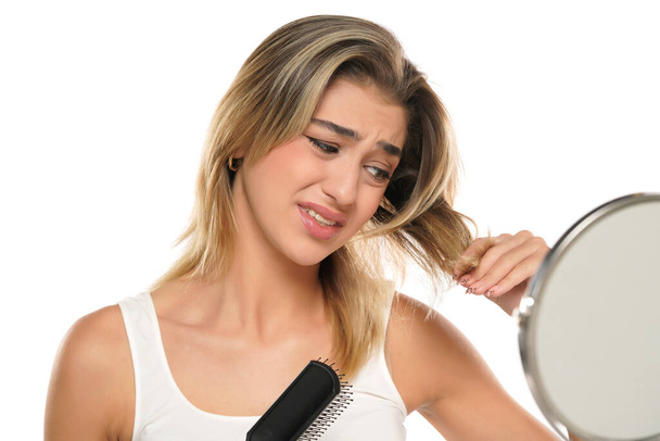 Young nervous unhappy woman brushing hair in front of a mirror on a white studio background - Foto, Imagem