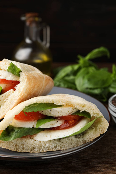 Delicious pita sandwiches with mozzarella, tomatoes and basil on wooden table - Photo, image