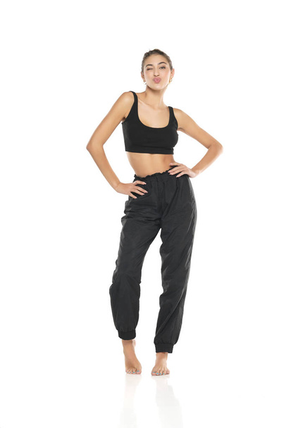 a young barefeet woman in black sweatpants and a tank top on a white studio background - 写真・画像