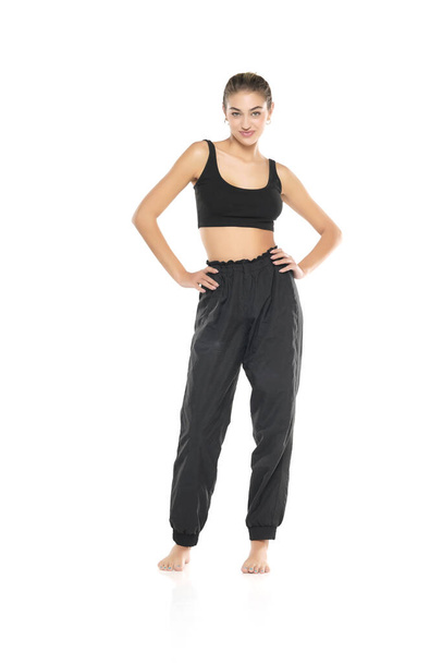 a young barefeet woman in black sweatpants and a tank top on a white studio background - Zdjęcie, obraz