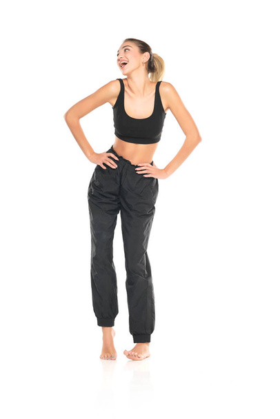 a young barefeet happy woman in black sweatpants and a tank top on a white studio background - Zdjęcie, obraz