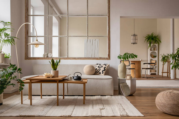 Creative composition of living room interior with modular sofa, beige rug, plants, vase with green leaves, pouf, stylish coffee table, big window, lamp and personal accessories. Home decor. Template.  - 写真・画像