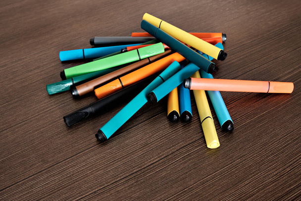 I pennarelli colorati per disegnare sono caoticamente sdraiati su un tavolo scuro. - Foto, immagini