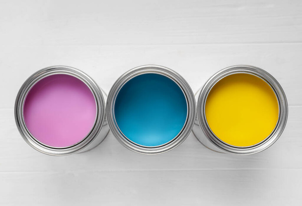 Cans of pink, light blue and yellow paints on white wooden table, flat lay - Фото, зображення