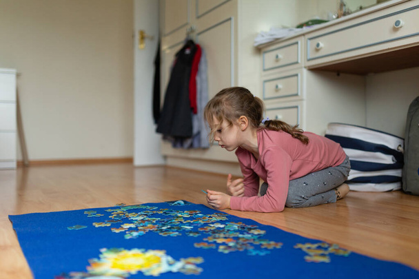 Klein meisje dat op de vloer zit en een puzzel oplost - Foto, afbeelding