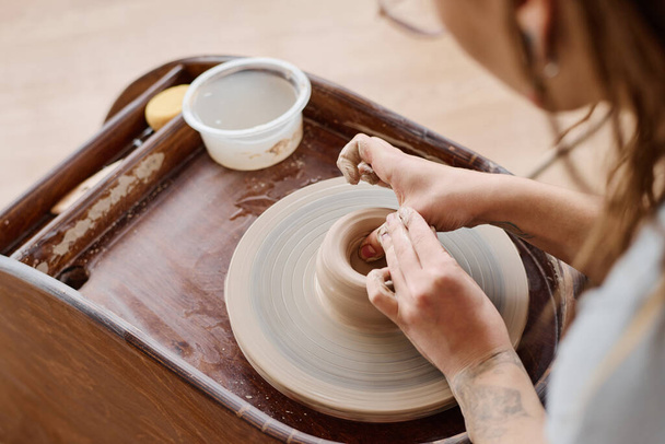 Руки молодой талантливой ремесленницы или гончара, формирующие верхнюю часть нового глиняного горшка или кувшина во время работы на гончарном круге в мастерской - Фото, изображение