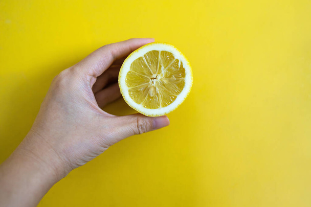 Hand holding fresh lemon slice on a yellow background. - Foto, immagini