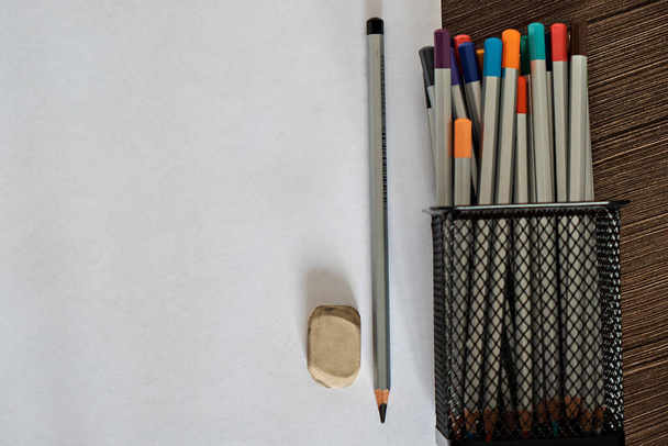 Metal bir tutacakta renkli kalemler ve silmek için ayrı bir lastik bant ve koyu beyaz arka planda siyah grafit kalemler.. - Fotoğraf, Görsel