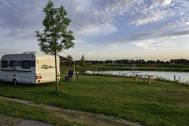 een caravan met de luifel is op een camping aan een meer tijdens de avond met zonsondergang - Foto, afbeelding