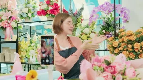 E-Commerce-Geschäft, eine junge weiße Floristin demonstriert und zeigt Blumenarrangements per Online-Live-Streaming mit Smartphone-Anwendung in hellen Blumenladen, schöne Blüten speichern.  - Filmmaterial, Video