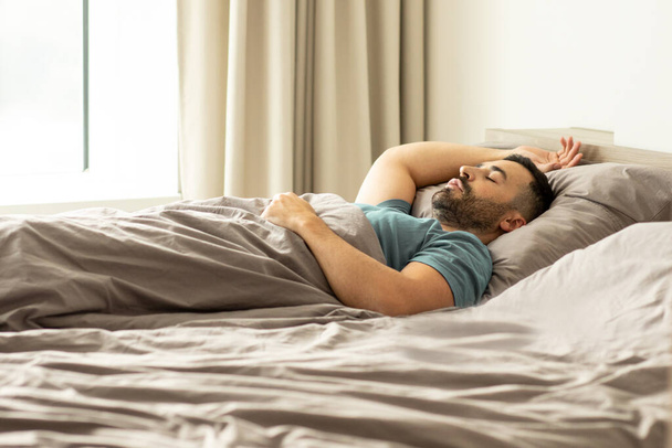 Pokojowy mężczyzna śpi, przykrywa się kocem, odpoczywa w wygodnym łóżku w domu, wolna przestrzeń. Głęboki sen męski, czas na odpoczynek i drzemkę - Zdjęcie, obraz