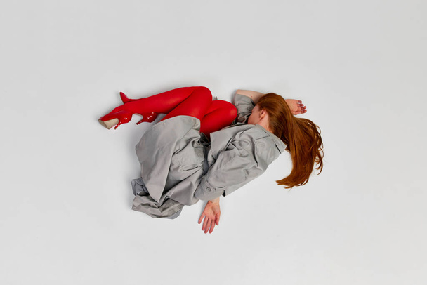 Impersonal human emotions. Stylish girl in grey coat and bright red tights moves over light background. Expressive fashion. Concept of art photography, beauty. Redhaired model in contemporary dance - Fotografie, Obrázek