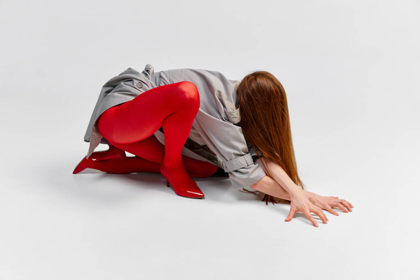 Impersonal human emotions. Stylish girl in grey coat and bright red tights moves over light background. Expressive fashion. Concept of art photography, beauty. Redhaired model in contemporary dance - Photo, image