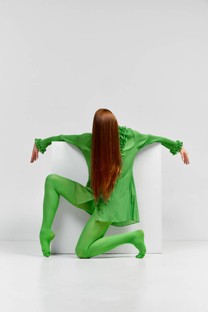 Dance. Avant-garde and experimental art style of human portrait. Unknown woman with long glossy red hair in green outfit posing over light background. Body language, faceless emotions concept - Fotografie, Obrázek