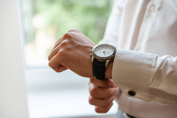 Un hombre con una camisa blanca sujeta la correa de un reloj caro en su mano - Foto, imagen
