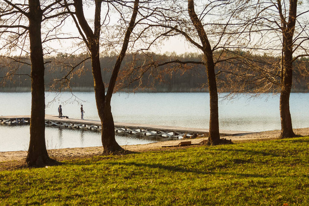A tó partján fák, móló és sziluettek a halászok egy napsütéses napon - Fotó, kép