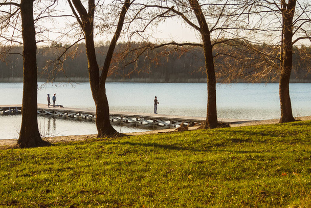 A tó partján fák, móló és sziluettek a halászok egy napsütéses napon - Fotó, kép