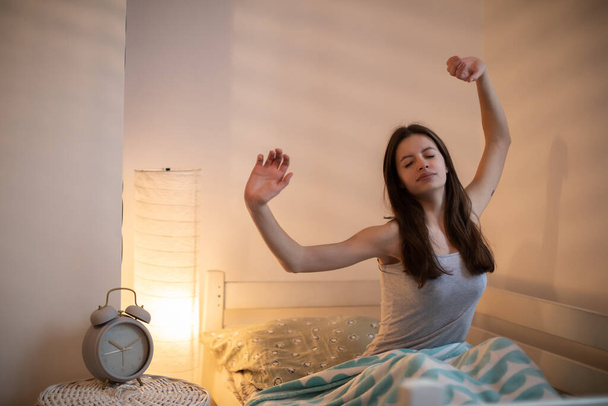 A girl with long hair on her bed stretches after sleeping. Bedroom in bright colors. - Foto, afbeelding
