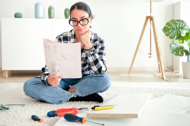 Egy nő, aki bútorokat szerel az otthonában egy felújítási projekt részeként. Különböző eszközöket használ. - Fotó, kép