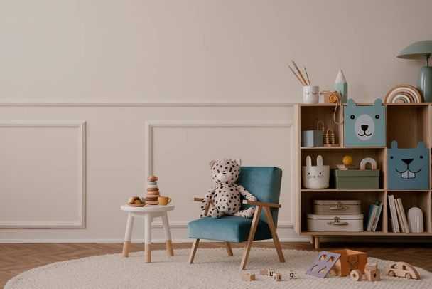 Minimalist composition of kid room interior with copy space, blue armchair, wooden sideboard, beige rug, plush toys, wooden blockers, wall with stucco and personal accessories. Home decor. Template. - Фото, изображение