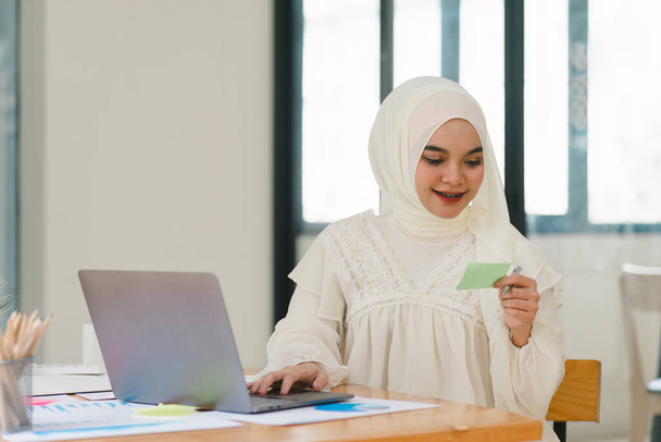 Bella donna d'affari musulmana che indossa un hijab sta lavorando diligentemente al suo computer, mostrando professionalità e impegno per il suo lavoro. - Foto, immagini