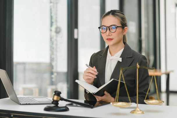 A businesswoman and lawyers are discussing contract papers with a brass scale on a desk in an office. The concepts of law, legal services, advice, justice, and real estate are being discussed - Photo, image