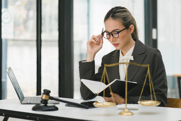 A businesswoman and lawyers are discussing contract papers with a brass scale on a desk in an office. The concepts of law, legal services, advice, justice, and real estate are being discussed - Photo, image
