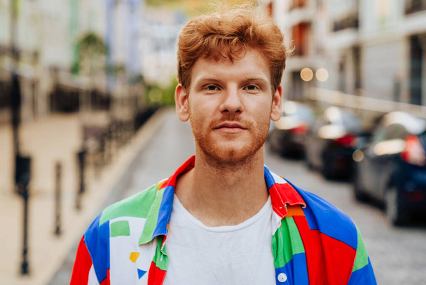 Portrait of young handsome calm redhead man with stubble in colorful shirt, standning on the street - Valokuva, kuva