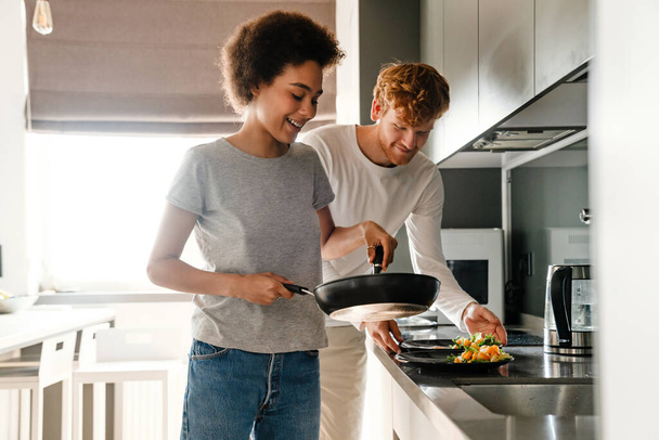 Young multinational couple smiling while cooking breakfast together at home - Valokuva, kuva