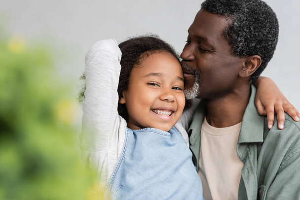 Afrikanisch-amerikanischer Großvater küsst Kopf der glücklichen Enkelin zu Hause  - Foto, Bild