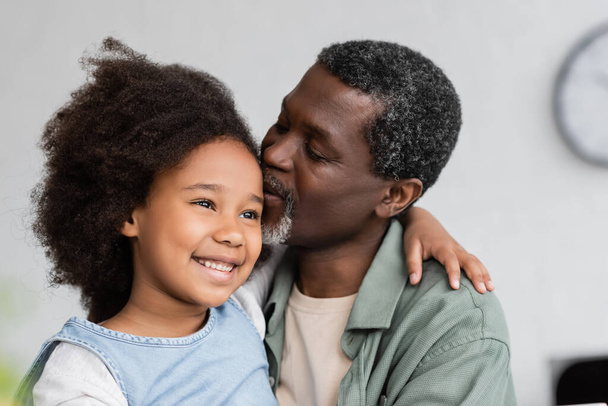 african american grandfather kissing head of cheerful granddaughter with curly hair  - Foto, afbeelding