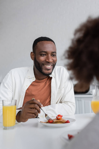 feliz afroamericano hombre desayunando y mirando rizado hija en cocina  - Foto, imagen
