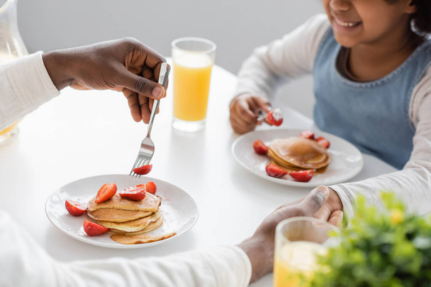 cropped view of cheerful african american girl holding hands with father during breakfast  - Фото, зображення