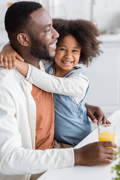 curly african american girl smiling while hugging happy father at home  - Foto, imagen