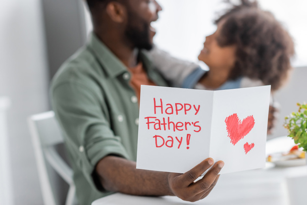africano americano hombre celebración de la tarjeta de felicitación con feliz padres día letras cerca de rizado hija en fondo borroso  - Foto, imagen
