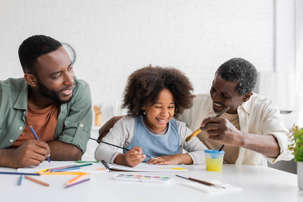 Веселі афроамериканські батьки малюють з дитиною вдома.  - Фото, зображення