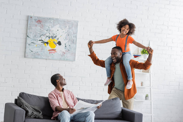 African american grandparent holding newspaper near son and granddaughter having fun at home  - Photo, Image