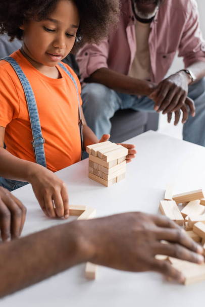 African american kid playing wood blocks game with blurred dad near grandfather at home  - Фото, изображение
