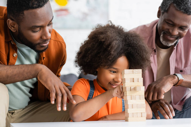 Kaygısız Afrikalı Amerikalı çocuk evde büyükbaba ve büyükbabasıyla tahta bloklar oynuyor.  - Fotoğraf, Görsel