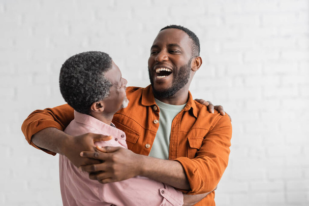 Positive african american son hugging mature father in living room  - Фото, зображення