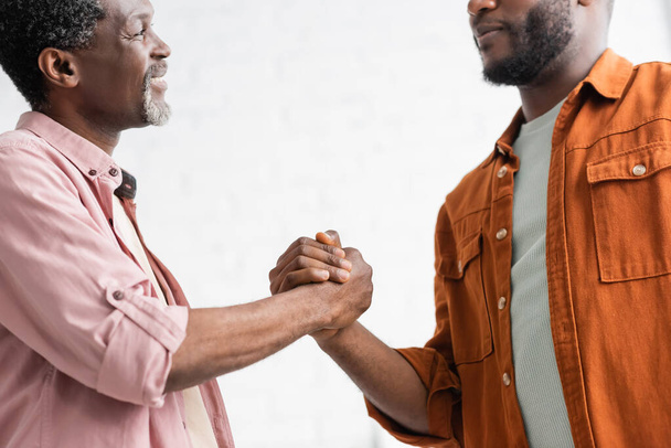 Улыбающийся африканский американец держит за руку взрослого сына дома - Фото, изображение