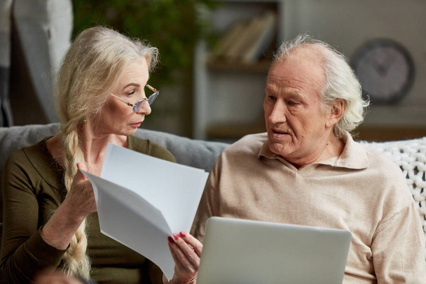 Focused middle aged retired couple, man and woman attentively looking on papers, bills, working on laptop at home. Using internet for payment. Concept of family, relationship, lifestyle, retirement - Fotó, kép