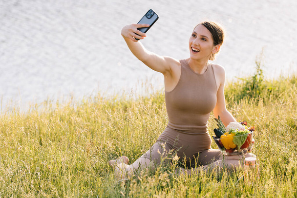 Happy sporty woman taking selfie with plate of fresh vegetables on the outdoors - Фото, зображення