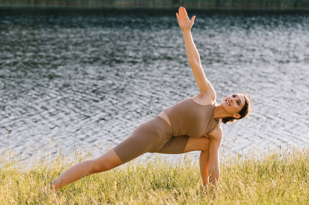Happy woman practicing yoga on the outdoors by the river - Фото, изображение