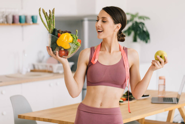 Portret van vrolijke sportieve vrouw met appel en bord verse groenten, gezond eetconcept - Foto, afbeelding