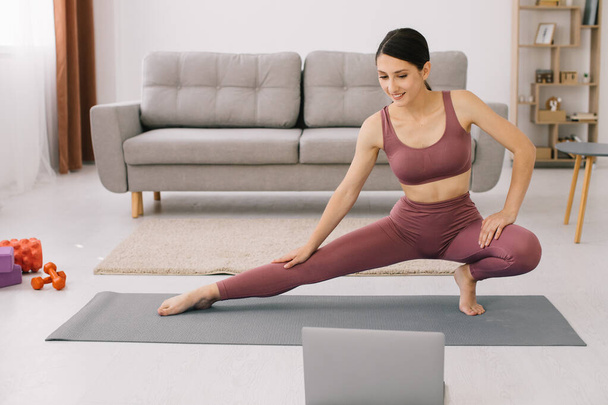Giovane donna sportiva che pratica yoga davanti al computer portatile, guardando tutorial online. - Foto, immagini