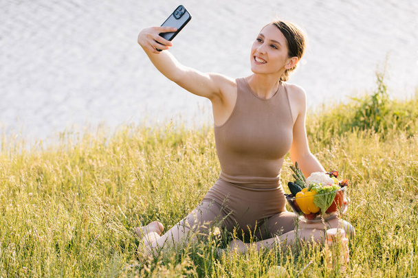 Happy sporty woman taking selfie with plate of fresh vegetables on the outdoors - Foto, immagini